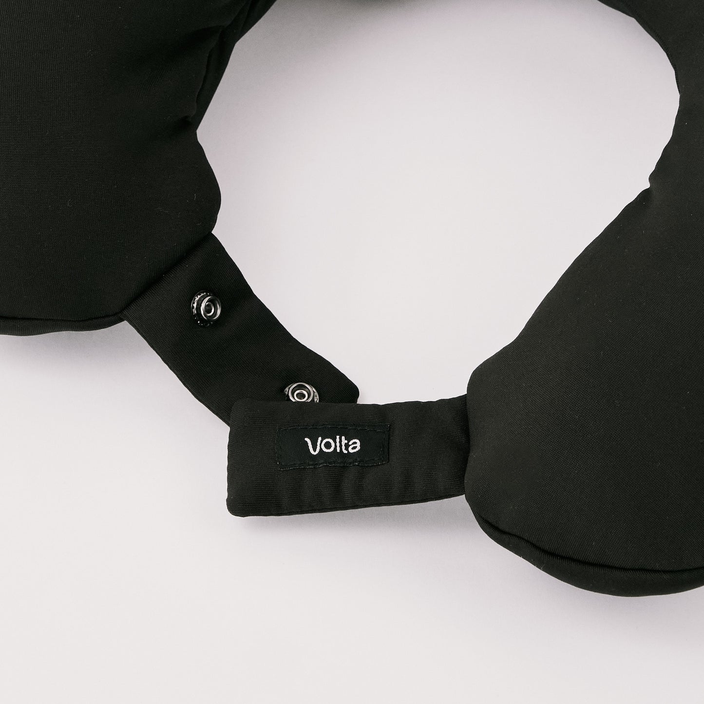 Close-up of black travel neck pillow showing snap buttons and the Volta brand label, highlighting the secure fastening feature.