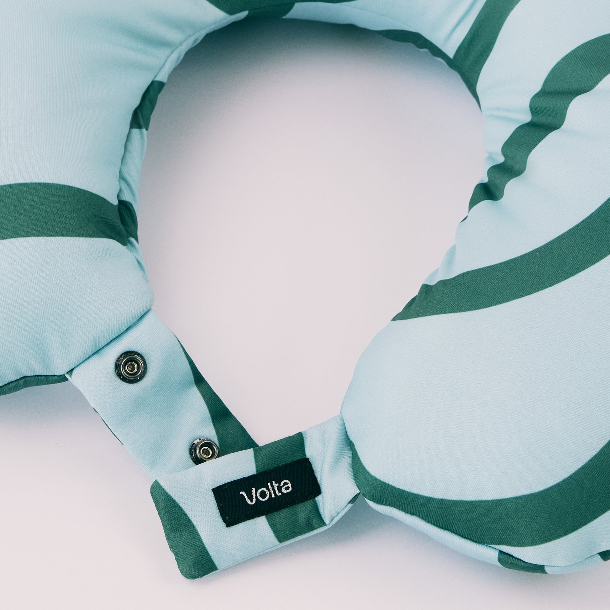 Close-up of snap buttons and the brand label on a blue-green striped travel neck pillow, showing its functional closure.