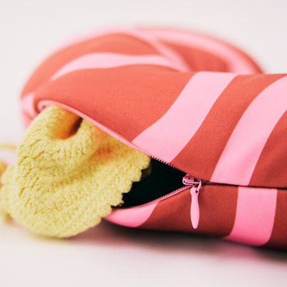 Red and pink travel neck pillow with clothes stored inside, showing the stuffable zipper feature for extra storage.